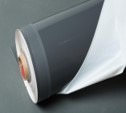 A close-up of a roll of black and white film or plastic material, partially unrolled on a dark surface. | GenFlex