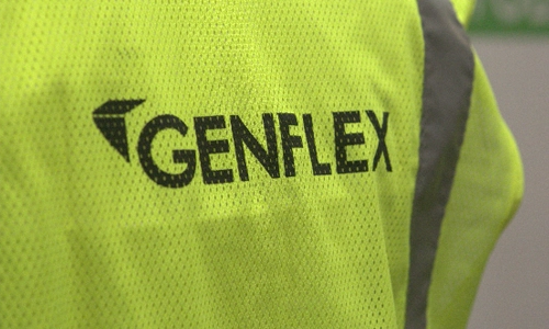 A close-up of a neon yellow safety vest with the word GENFLEX printed in bold black letters and a reflective gray stripe on the right side. | GenFlex